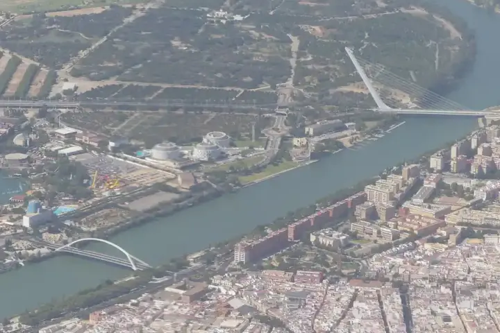 High-altitude aerial photograph of the urban landscape of Seville and surrounding agricultural land under bright daylight.