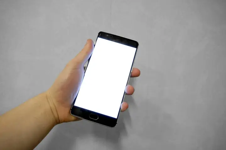 Hand holding a smartphone with a blank white screen