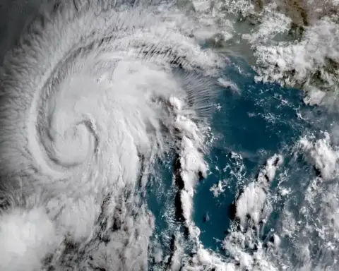 Enhanced geocolor satellite image of a circular tropical cyclone with dense central cloud tops over open ocean waters.
