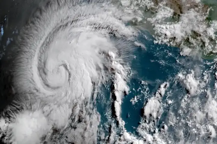 Enhanced geocolor satellite image of a circular tropical cyclone with dense central cloud tops over open ocean waters.
