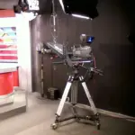 Television news studio camera positioned beside professional lighting and broadcast production equipment