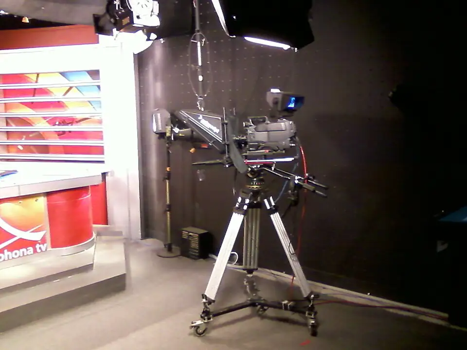 Television news studio camera positioned beside professional lighting and broadcast production equipment