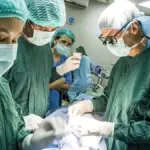 Specialized surgical transplant team performing complex surgery in an operating theater under overhead lights.