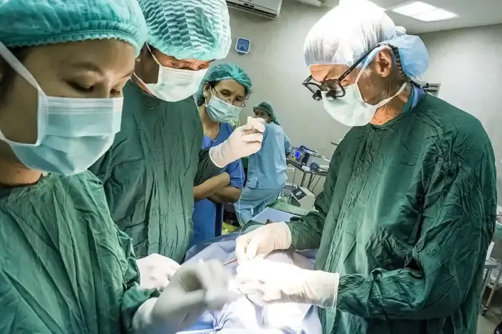 Specialized surgical transplant team performing complex surgery in an operating theater under overhead lights.