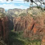 Towering red and white sandstone cliffs of Angels Landing rising above the forested canyon floor in Zion National Park.