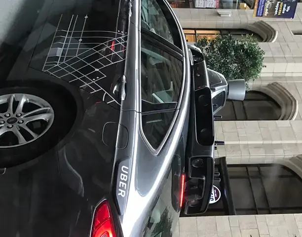 A dark Uber test car parked curbside with an automated navigation rig and lidar spinning sensor mounted on the roof.