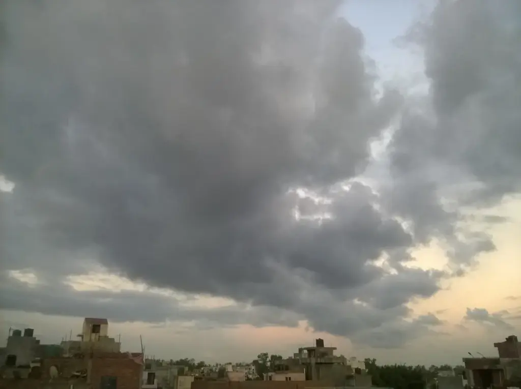 Photograph of heavy, dark monsoon rain clouds gathering over an open landscape in Delhi.