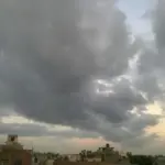 Photograph of heavy, dark monsoon rain clouds gathering over an open landscape in Delhi.