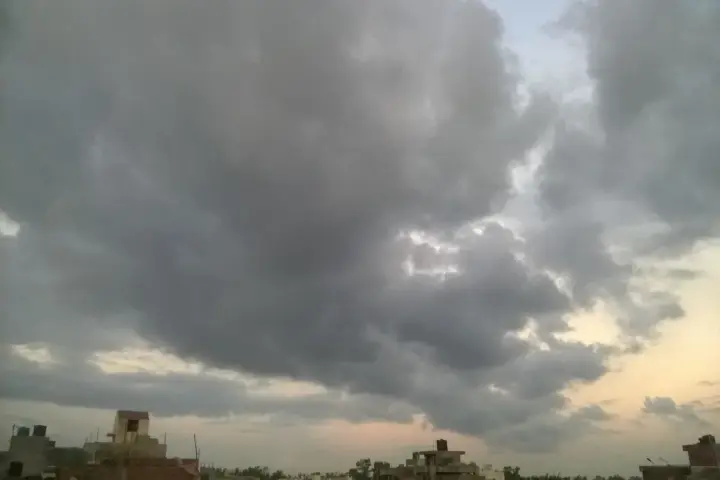 Photograph of heavy, dark monsoon rain clouds gathering over an open landscape in Delhi.