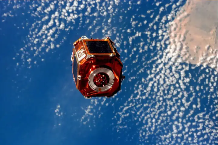Photograph taken from space showing an orbital satellite deployed against the blue curve of Earth.