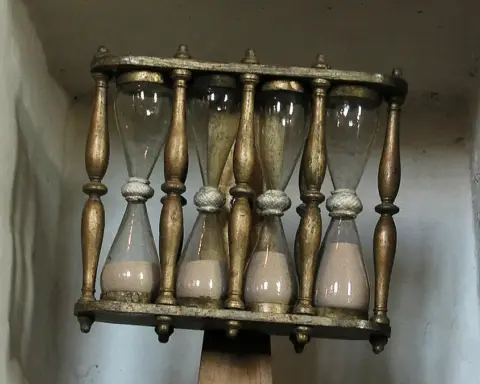 A glass hourglass in a wooden frame used for traditional timekeeping.