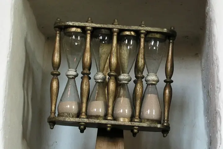 A glass hourglass in a wooden frame used for traditional timekeeping.