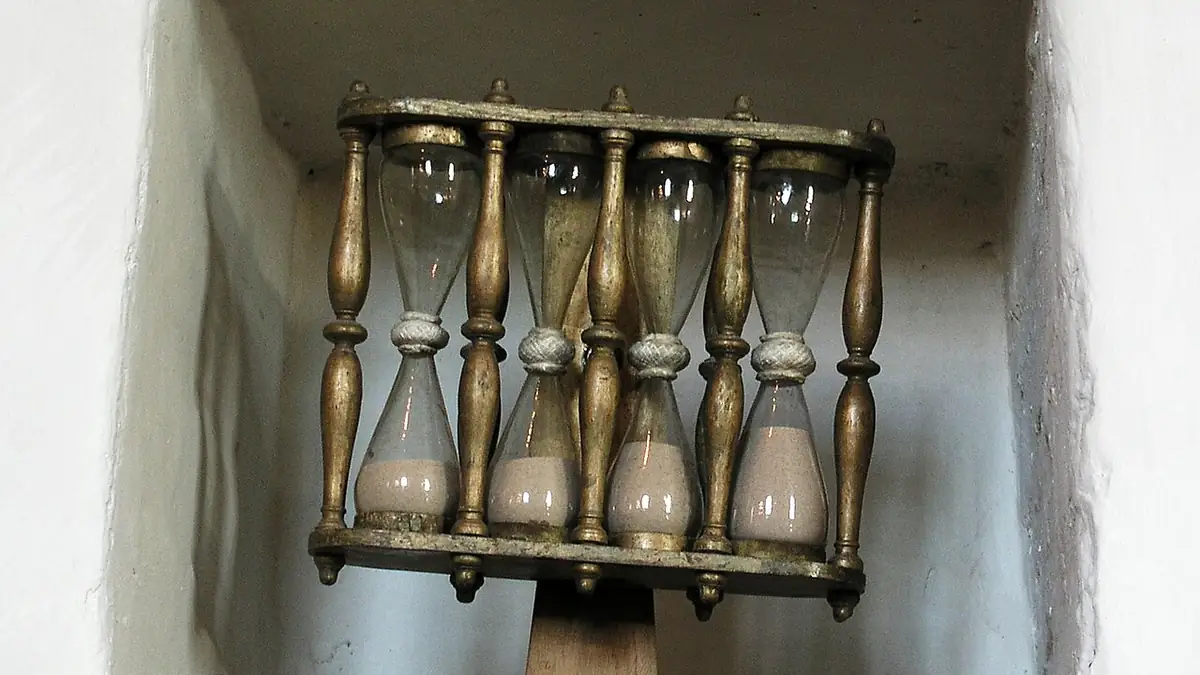 A glass hourglass in a wooden frame used for traditional timekeeping.