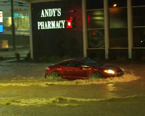 Street flooded with deep yellowish-brown water, a car driving through with splashes