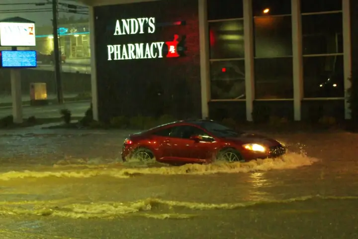 Street flooded with deep yellowish-brown water, a car driving through with splashes