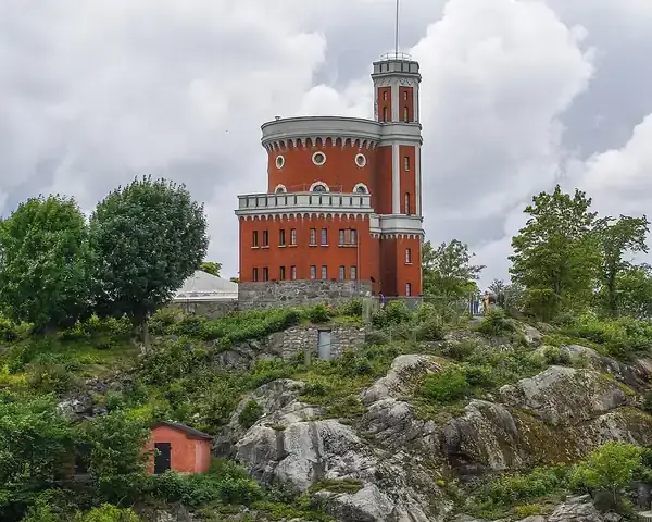 Historic castle-like structure on a rocky hill with a Swedish flag flying from the tower, cloudy sky