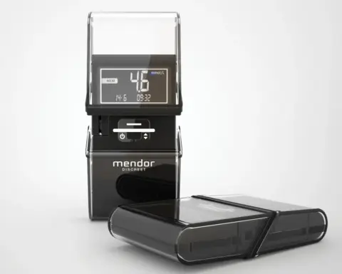 Photograph of a digital blood glucose meter with a test strip and detachable components on a white background.