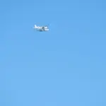 A Cessna 208 Caravan aircraft flying over coastal water, representing the type of turboprop aircraft used in autonomous flight testing like Joby's cross-US demonstration.