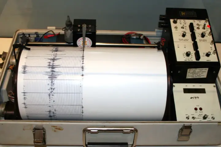 Analog rotating seismograph drum with stylus recording seismic waveform lines on paper