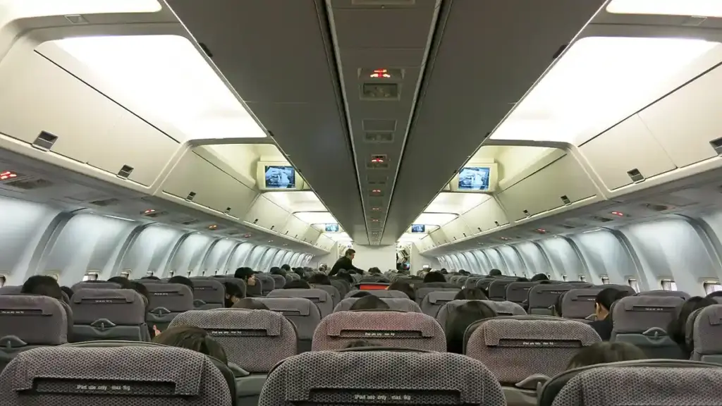 Interior view of a commercial passenger airplane cabin with rows of passenger seats and overhead bins