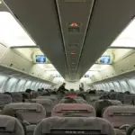 Interior view of a commercial passenger airplane cabin with rows of passenger seats and overhead bins