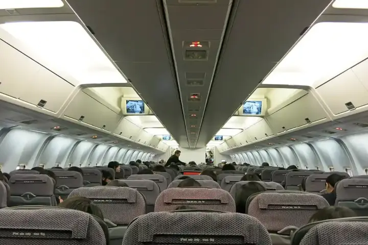 Interior view of a commercial passenger airplane cabin with rows of passenger seats and overhead bins