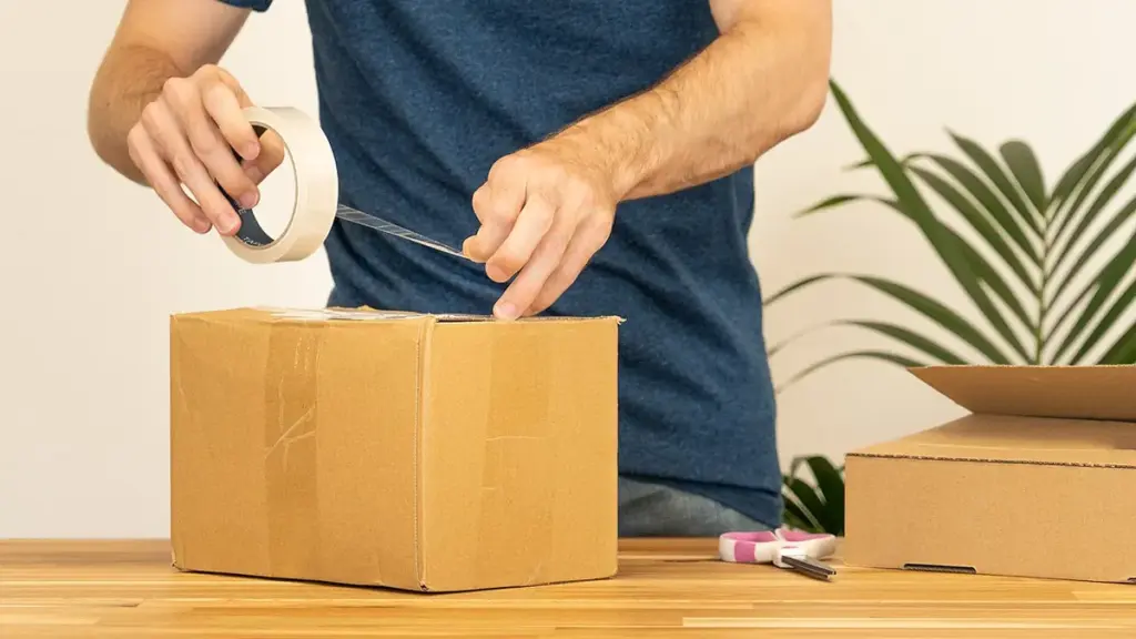 Hands sealing a cardboard shipping parcel with tape before delivery