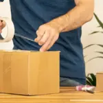 Hands sealing a cardboard shipping parcel with tape before delivery