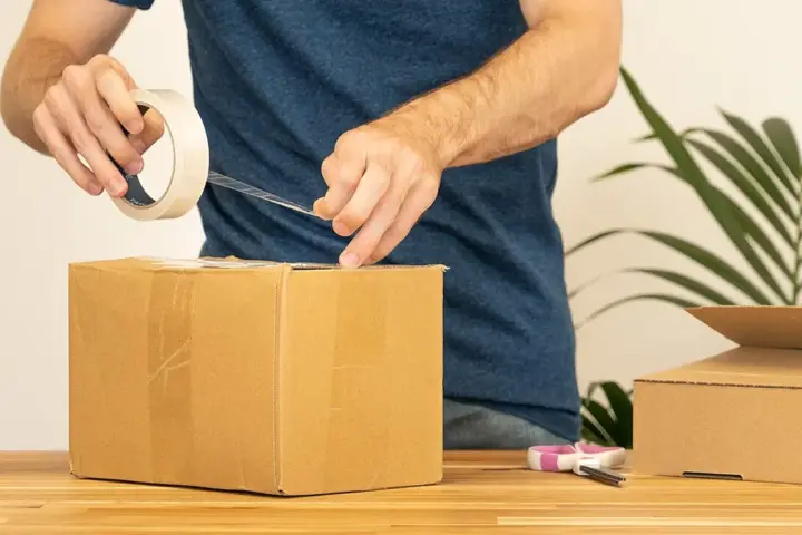 Hands sealing a cardboard shipping parcel with tape before delivery