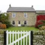 Garden gate beside a stone wall and green space in an English village