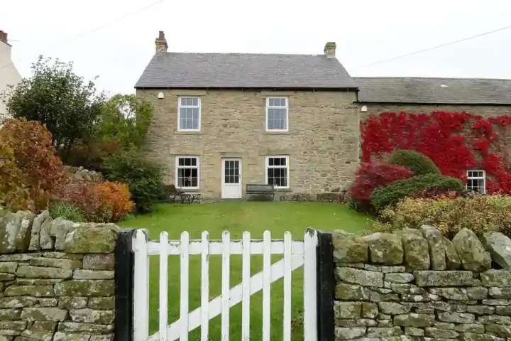 Garden gate beside a stone wall and green space in an English village