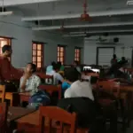 Group of Indian students seated at wooden study desks inside an academic classroom setting.