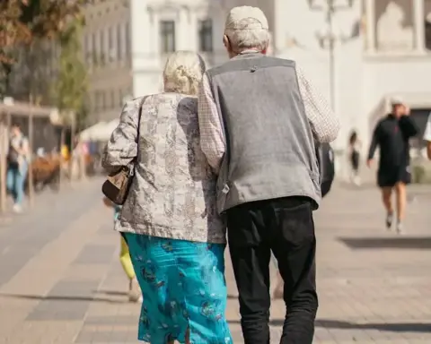 An older couple walks together on a city pavement, representing pensioners weighing the Winter Fuel Payment opt-out deadline.
