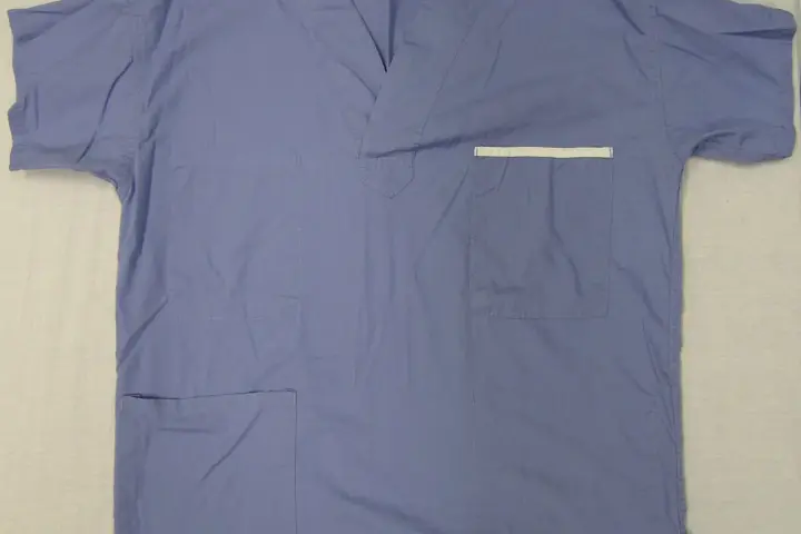 Blue medical scrub top photographed on a plain surface