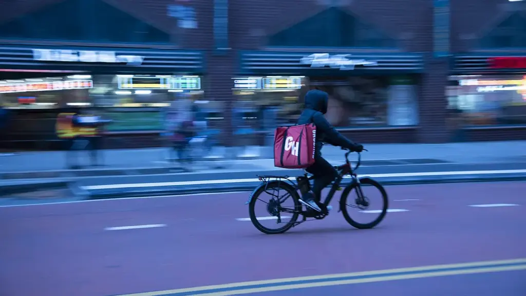 Food delivery worker riding a bicycle through New York City traffic with buildings and vehicles nearby.