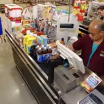 Family unloading groceries from a shopping cart at a checkout area, representing household retail spending.
