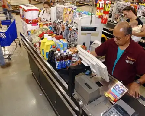 Family unloading groceries from a shopping cart at a checkout area, representing household retail spending.