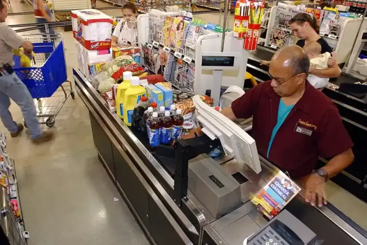 Family unloading groceries from a shopping cart at a checkout area, representing household retail spending.