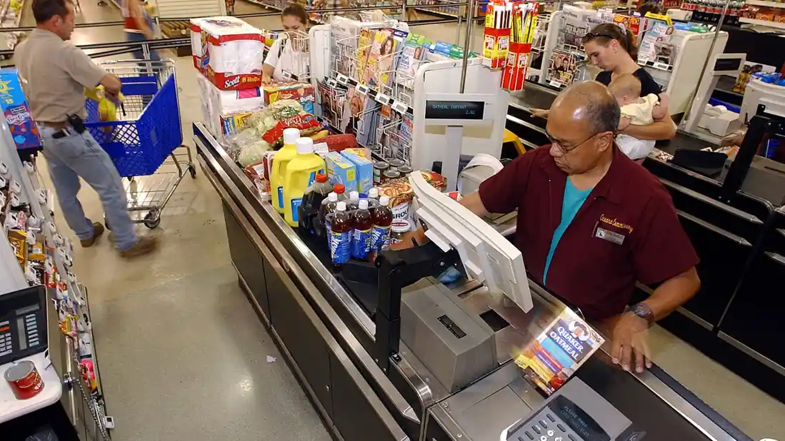 Family unloading groceries from a shopping cart at a checkout area, representing household retail spending.