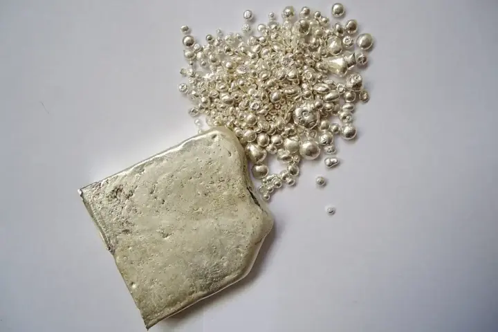 Silver ingot and fine silver granules photographed on a work surface