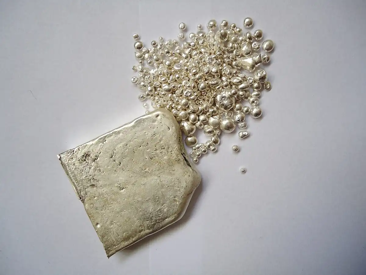 Silver ingot and fine silver granules photographed on a work surface
