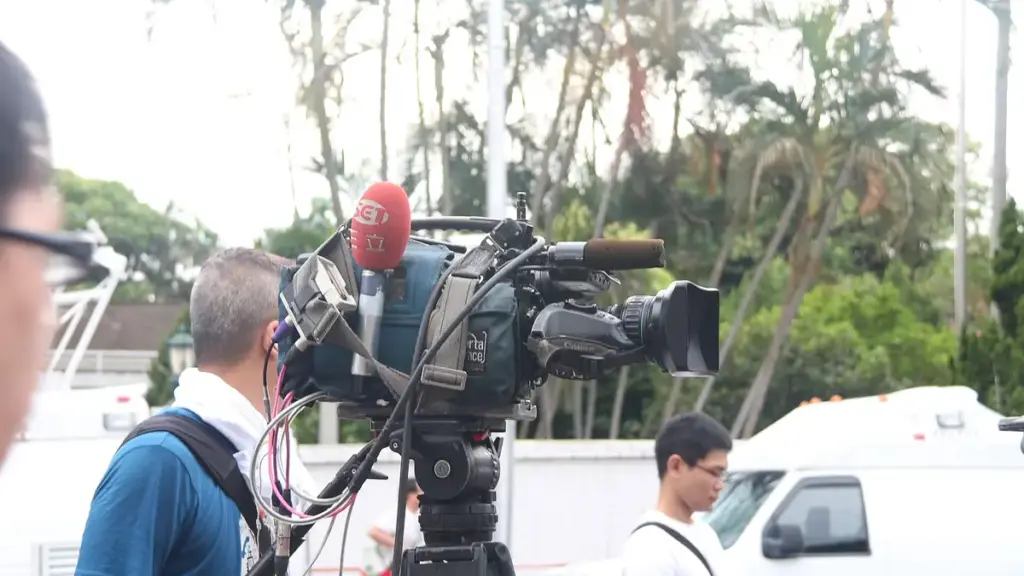 Professional broadcast video camera on a tripod with a large telephoto lens, used for documentary reporting context.