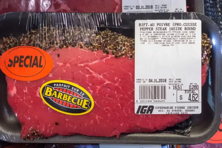Fresh cuts of uncooked beef and roasts packaged in plastic trays on supermarket shelves under store lighting.