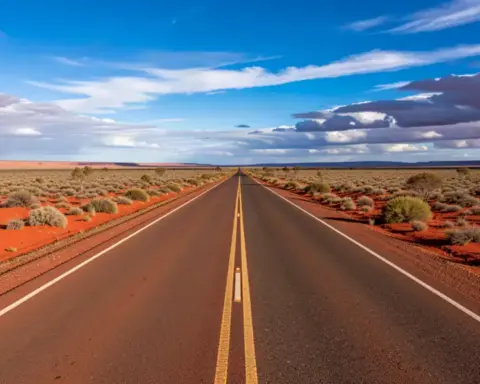 Two-lane asphalt road of the Stuart Highway cutting through arid red soil and low desert shrubs in Central Australia.