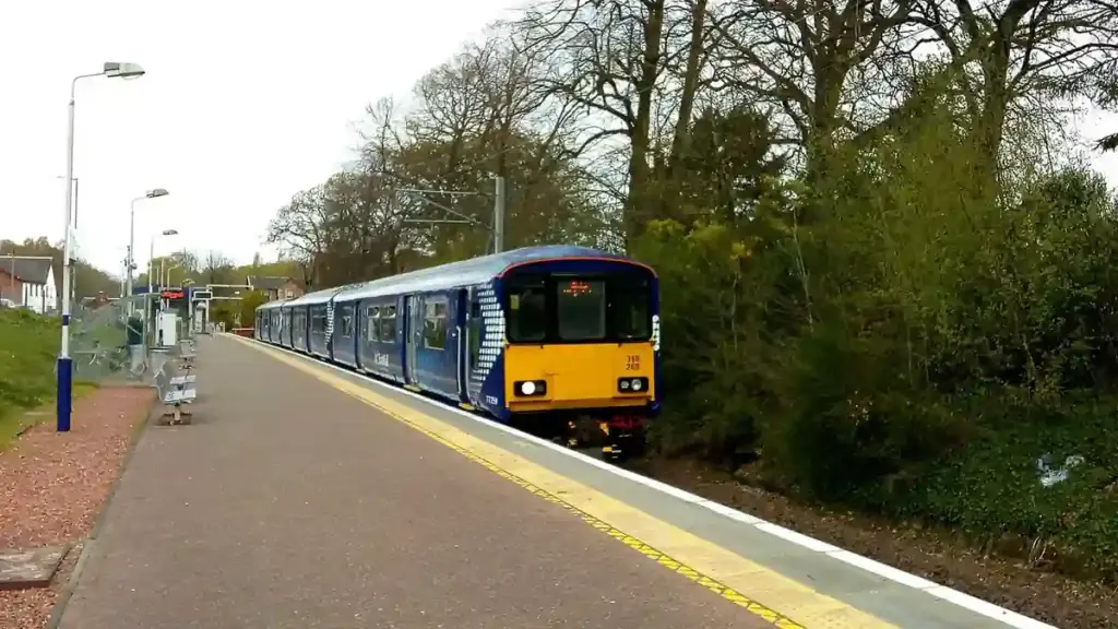 ScotRail train stopped beside a station platform with trees in the background