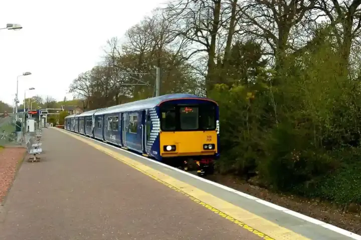 ScotRail train stopped beside a station platform with trees in the background