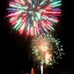 Colorful fireworks exploding in the night sky above a dark outdoor gathering area.