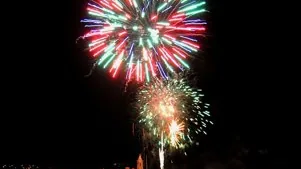 Colorful fireworks exploding in the night sky above a dark outdoor gathering area.