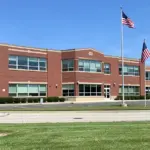 Front entrance and exterior brick facade of a public high school in suburban Michigan under daylight.