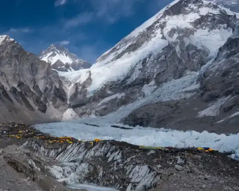 Bright yellow and orange mountaineering tents pitched directly on the rocky debris and ice pinnacles of Khumbu Glacier at Everest Base Camp